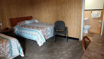 A room with two beds, a chair, a small table, and a toilet.