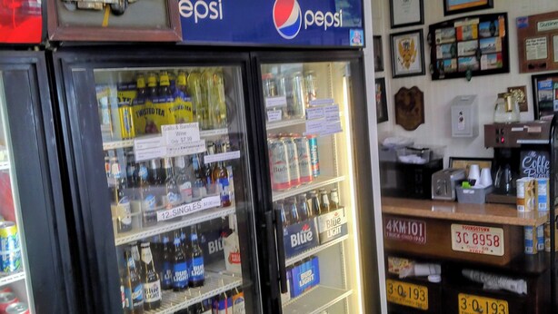 Un motel antiguo con un refrigerador vintage lleno de bebidas, un letrero de Pepsi y un cartel de bienvenida.