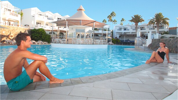 A pool area with a clear blue pool, lounge chairs, and a covered seating area. - Apartments Turbo Club (San Bartolomé de Tirajana)