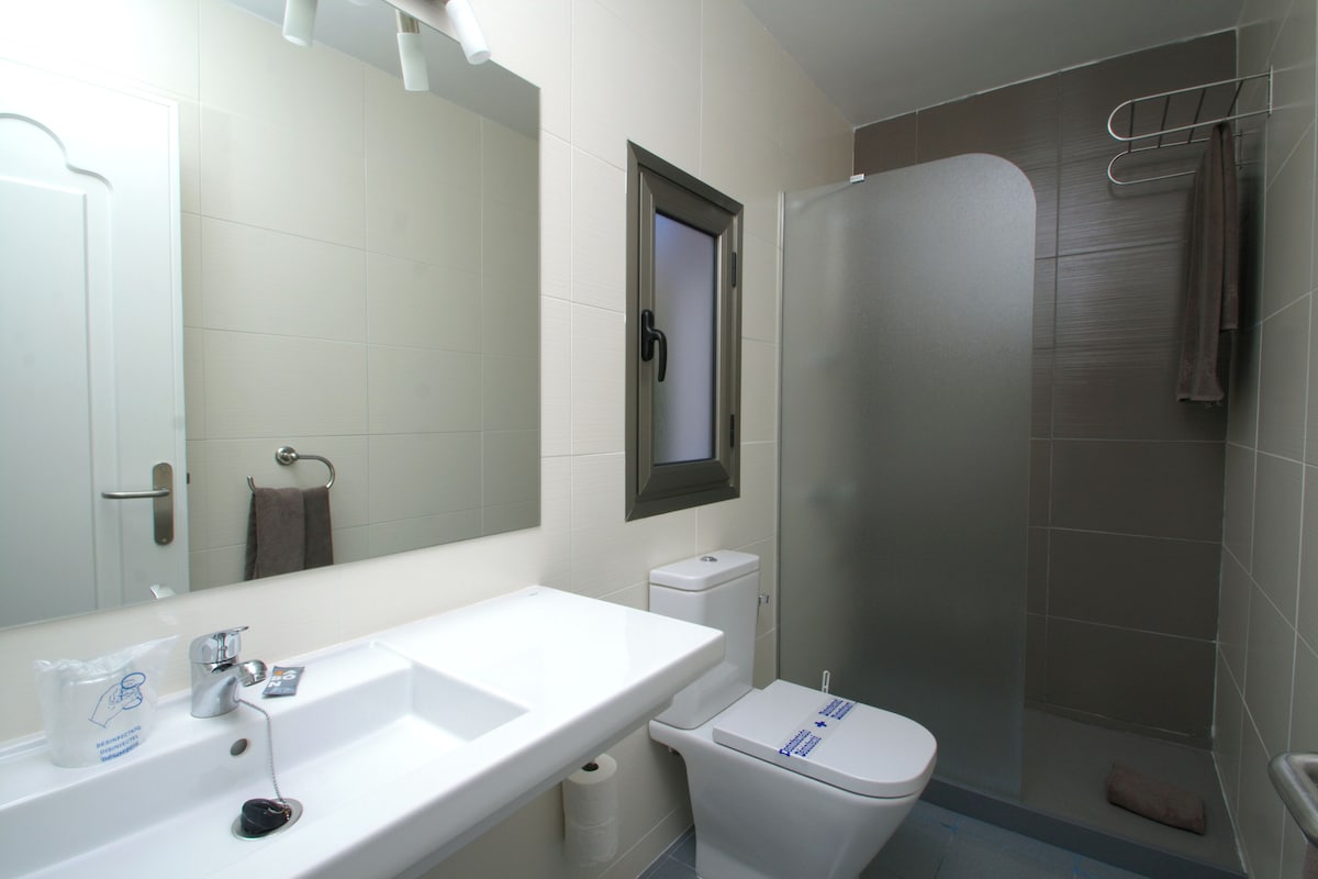 Un baño con lavamanos blanco, inodoro, ducha y toallero.