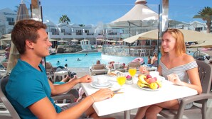 A dining table with a view of a swimming pool, surrounded by umbrellas and lounge chairs. - Apartments Turbo Club (San Bartolomé de Tirajana)