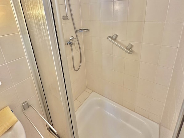 Une salle de bain dotée d’une douche à parois de verre, d’une baignoire blanche et d’une barre d’appui.