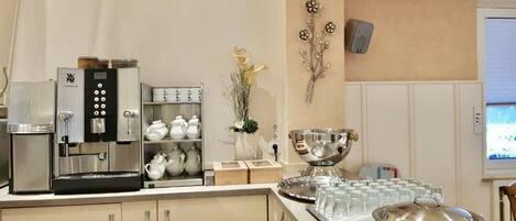 A kitchenette with a coffee machine, tea set, and a buffet setup with glasses and a silver bowl.