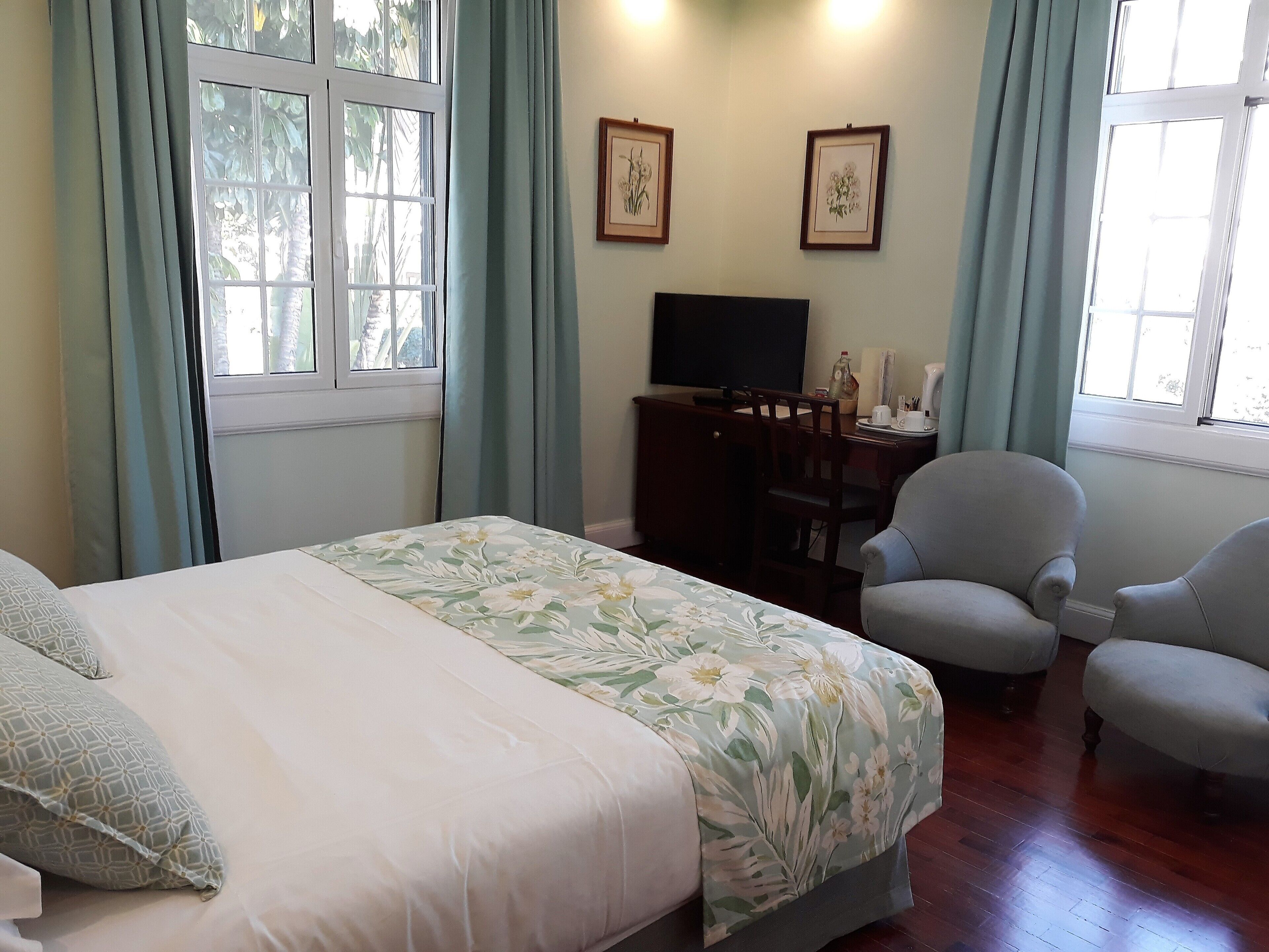 A bedroom with a bed, two chairs, a desk with a TV, and two framed pictures on the wall.