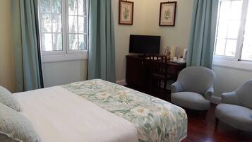 A bedroom with a bed, two chairs, a desk with a TV, and two framed pictures on the wall.