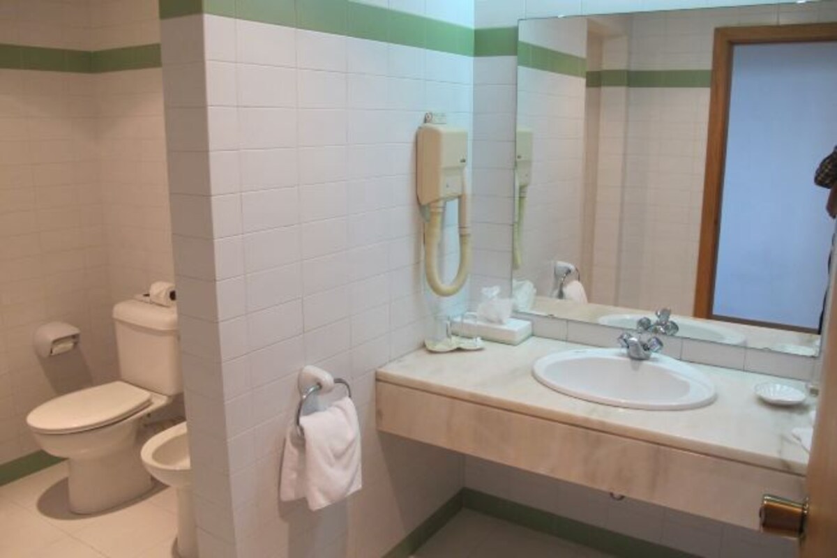 A bathroom with a toilet, bidet, sink, and mirror.
