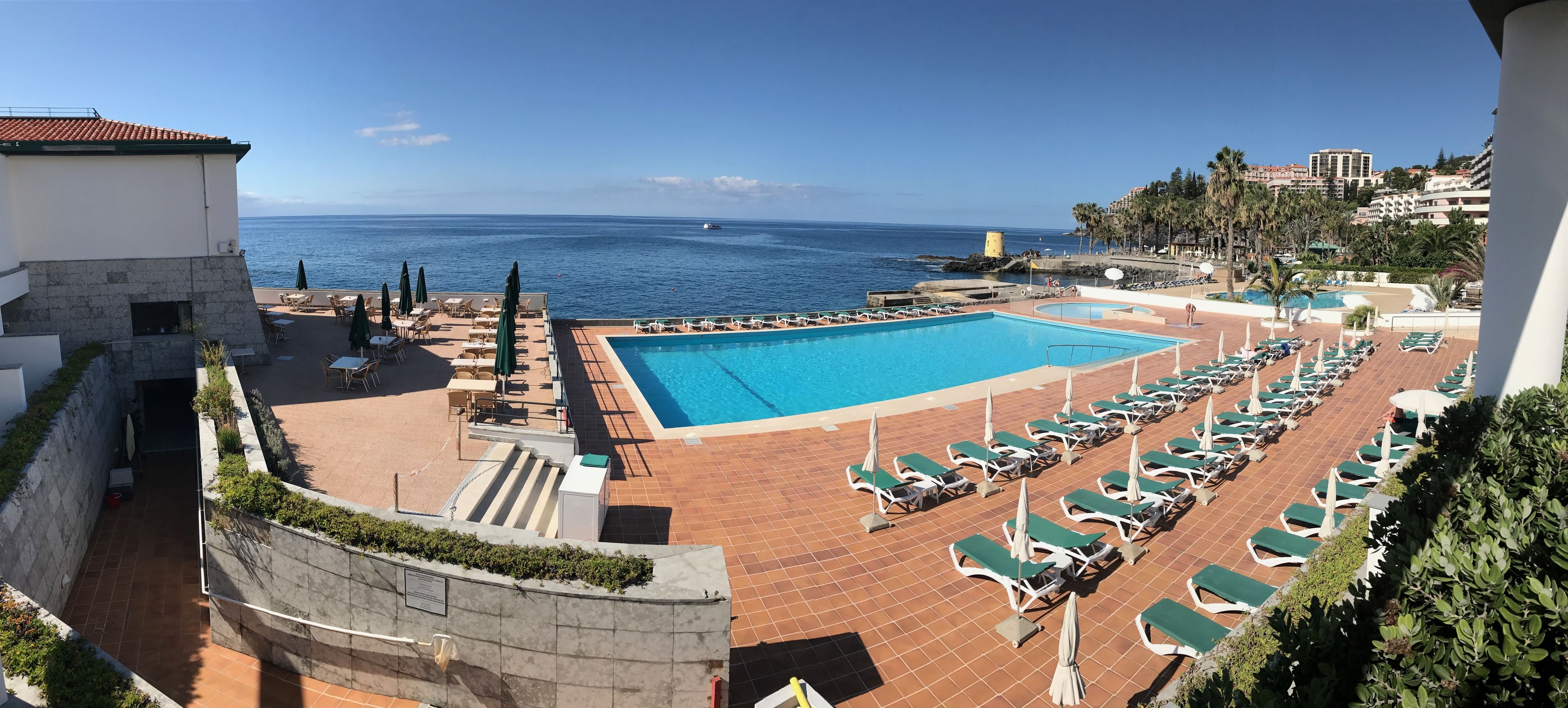 A resort pool area with a view of the sea, lounge chairs, and a swimming pool.