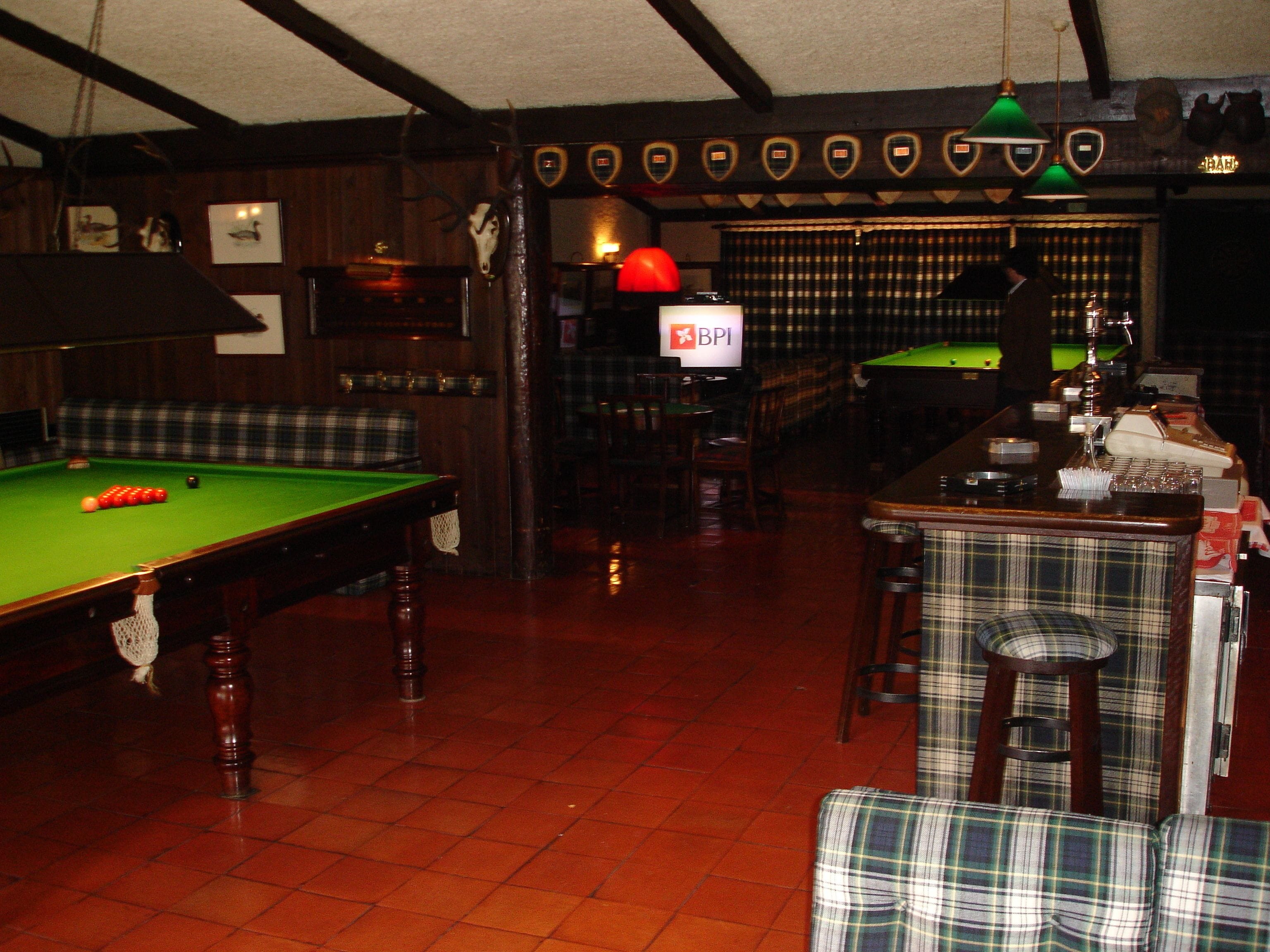 A billiards room with a pool table, a bar area, and a seating area with a plaid couch.