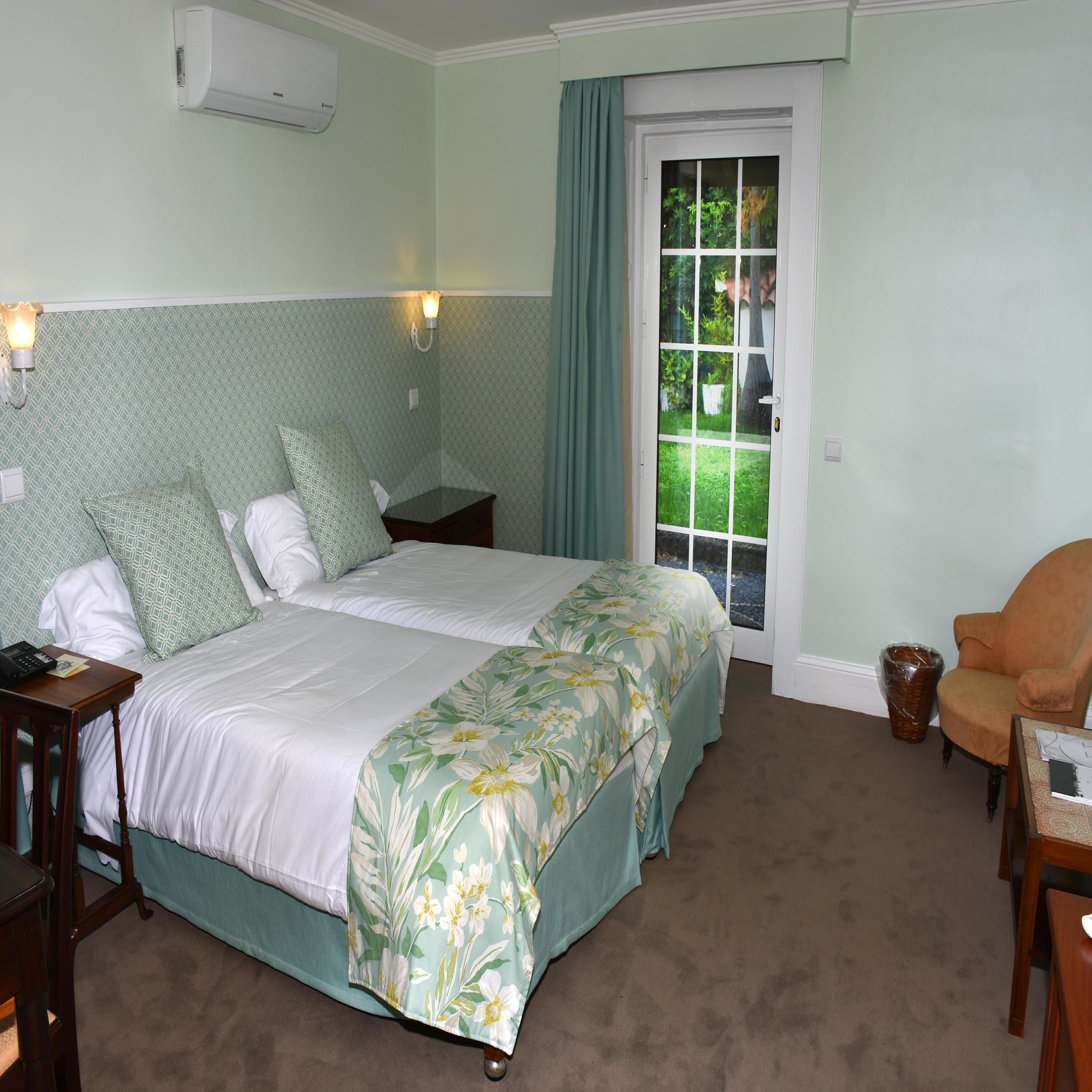 A neatly arranged bedroom with a bed, bedside tables, a chair, and a window with a view of greenery.