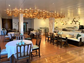 A spacious dining area with multiple tables and chairs, a central seating area with a sofa, and a kitchen in the background.