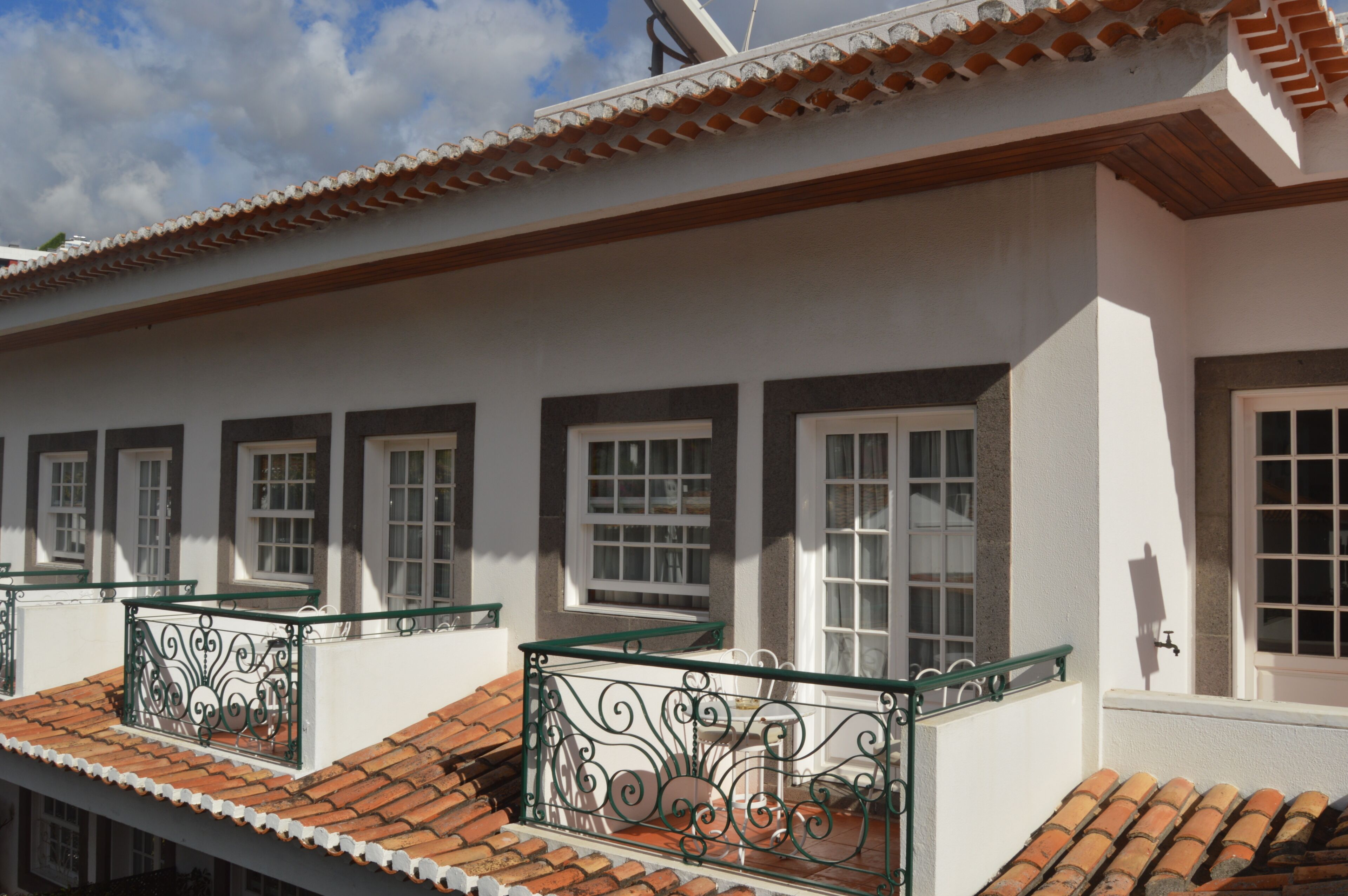 A building with multiple windows, a tiled roof, and a balcony with a metal railing.