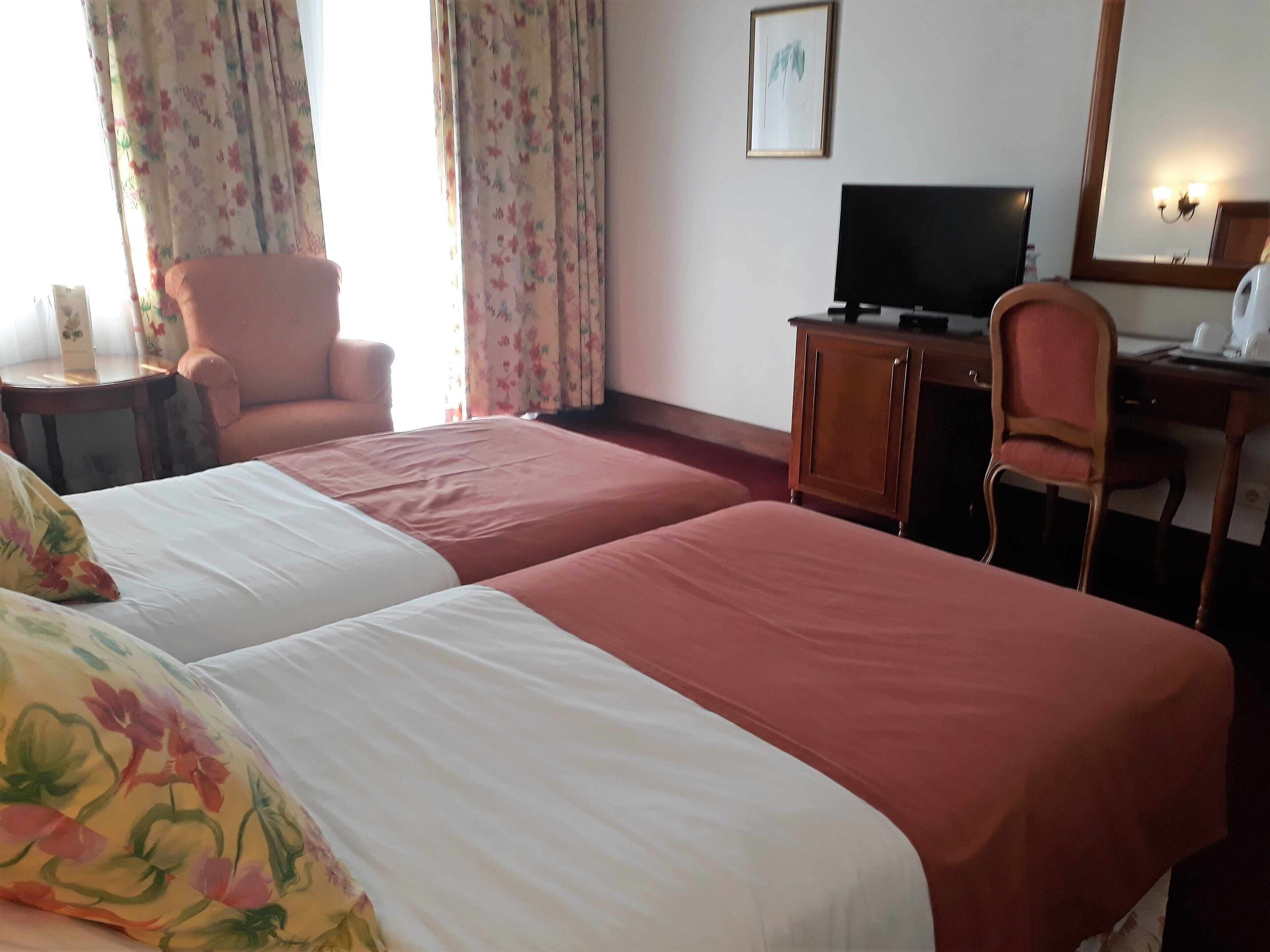 Une chambre d’hôtel avec deux lits, un bureau, une chaise, une télévision et un miroir.