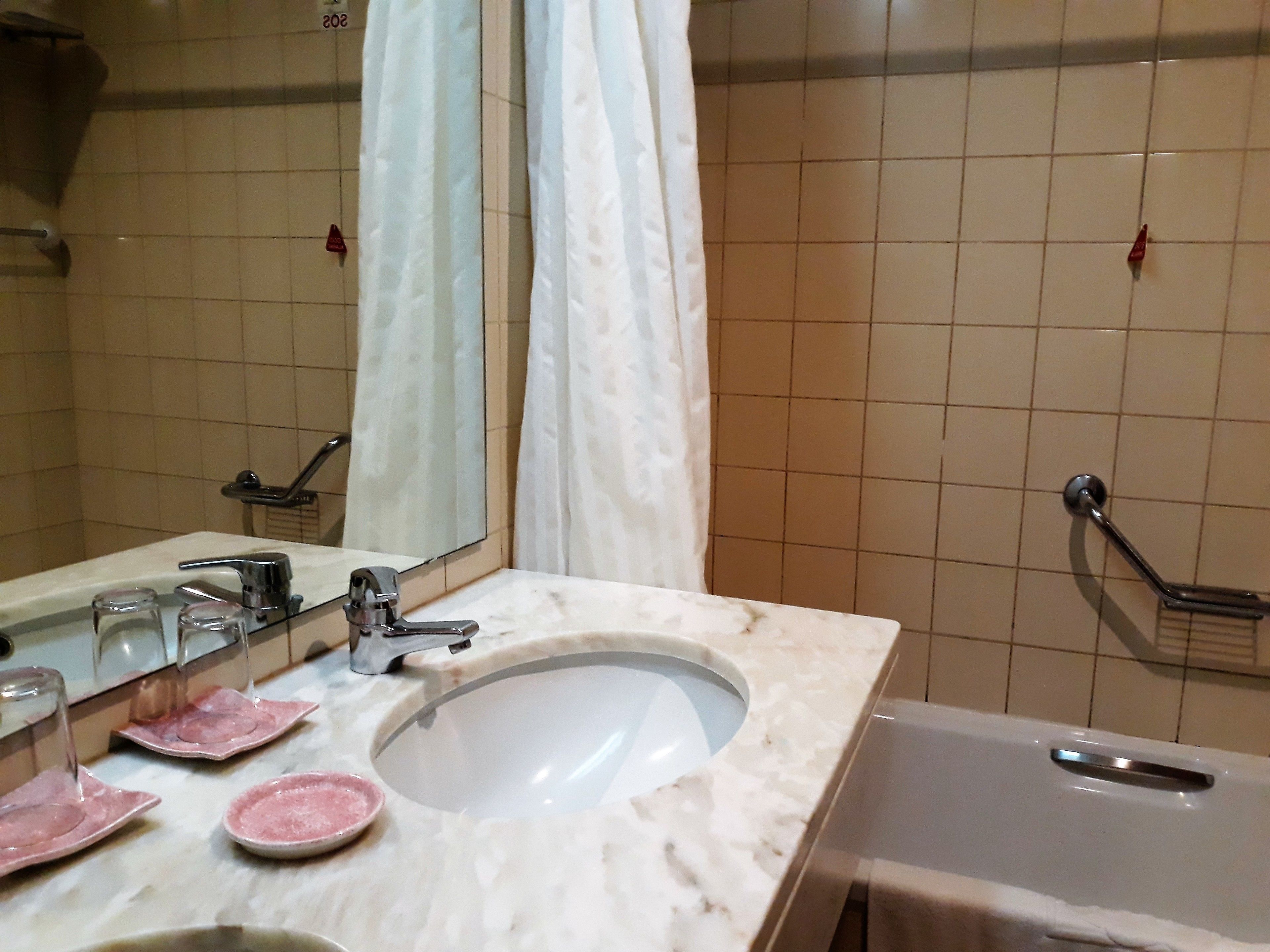 Un bagno con lavabo in marmo, uno specchio, una doccia con maniglione e un portasciugamani.