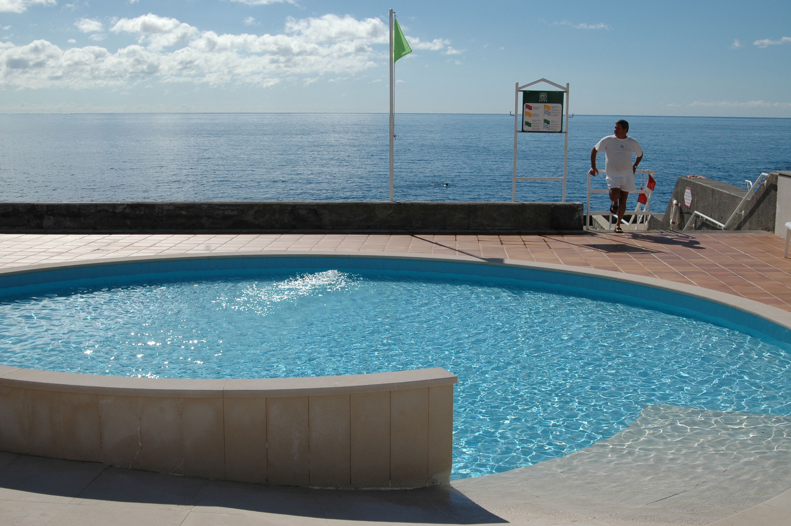 Una piscina amb vistes al mar, una bandera i un cartell.