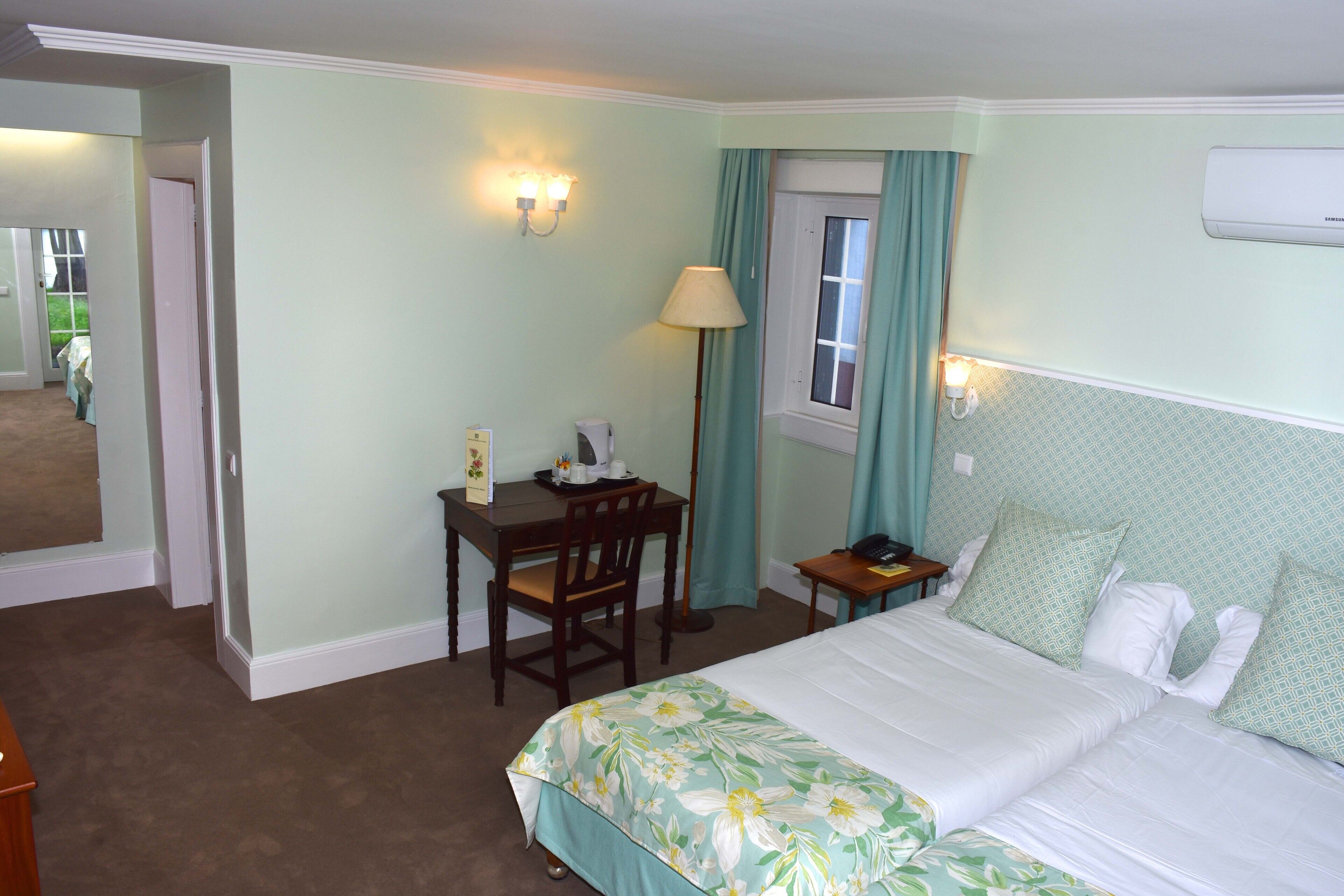 Ein Hotelzimmer mit Bett, Schreibtisch, Stuhl, Lampe und einem Fenster mit Vorhängen.
