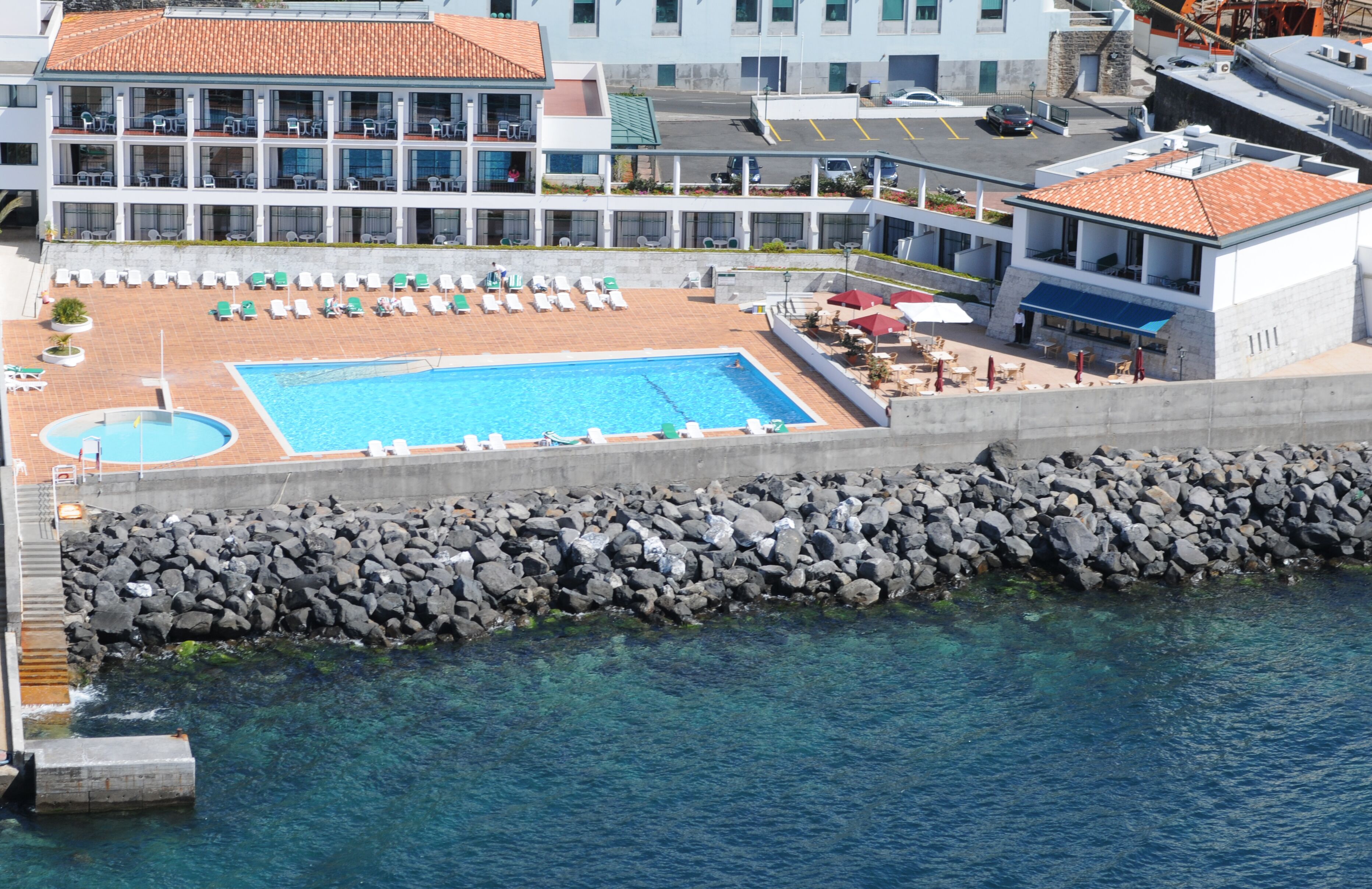 A hotel with a rooftop pool, lounge chairs, and a view of the sea.
