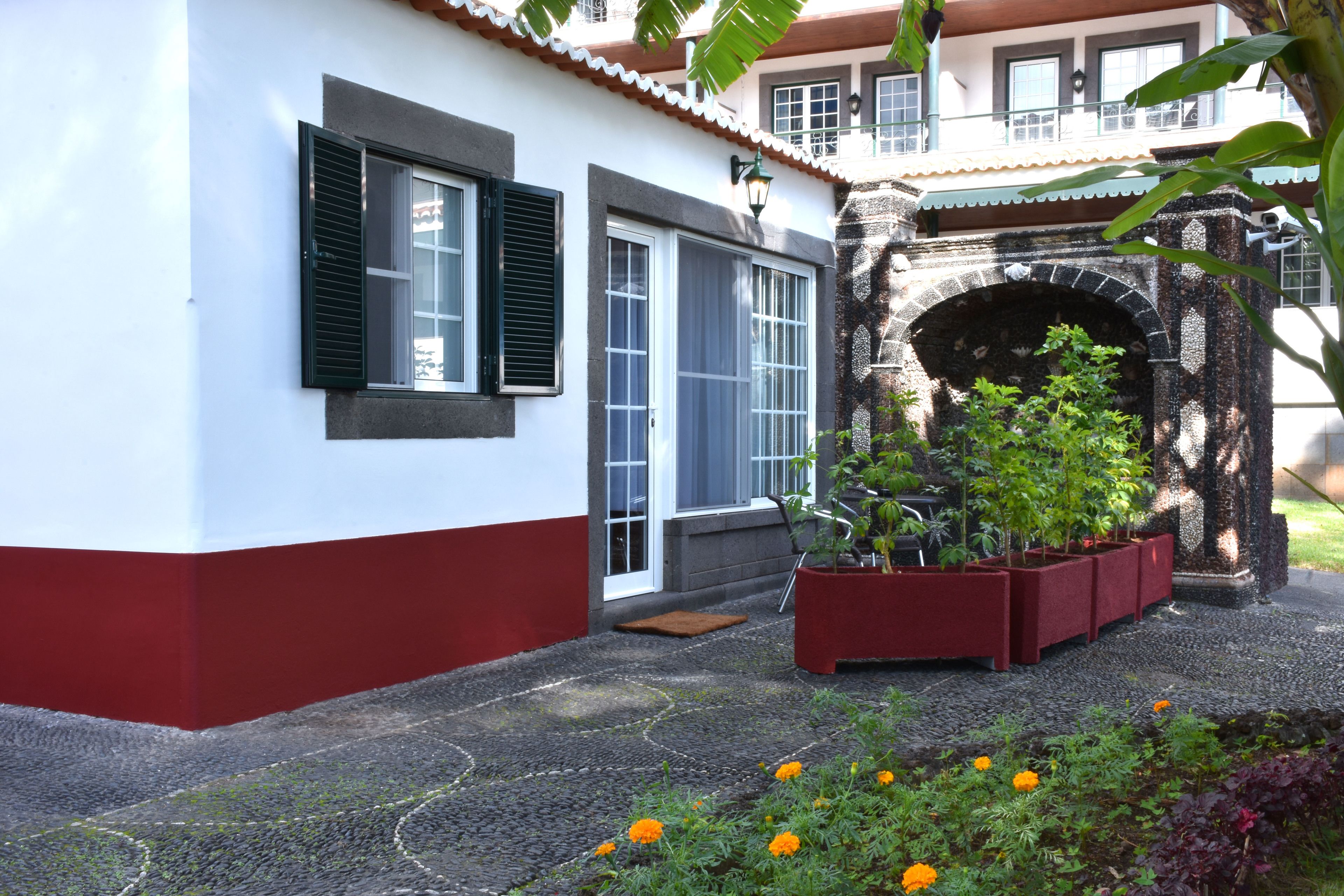 Un bâtiment à la façade blanche et rouge, doté d’une arche en pierre et d’un jardin où poussent des fleurs oranges.