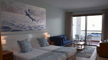 Habitación de hotel con dos camas, un sofá, un balcón con vistas y un cuadro de un pez.