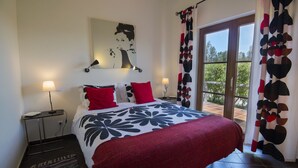 A bedroom with a bed, two bedside tables, a wall-mounted lamp, and a window with curtains. - Casa Vicentina (Aljezur)