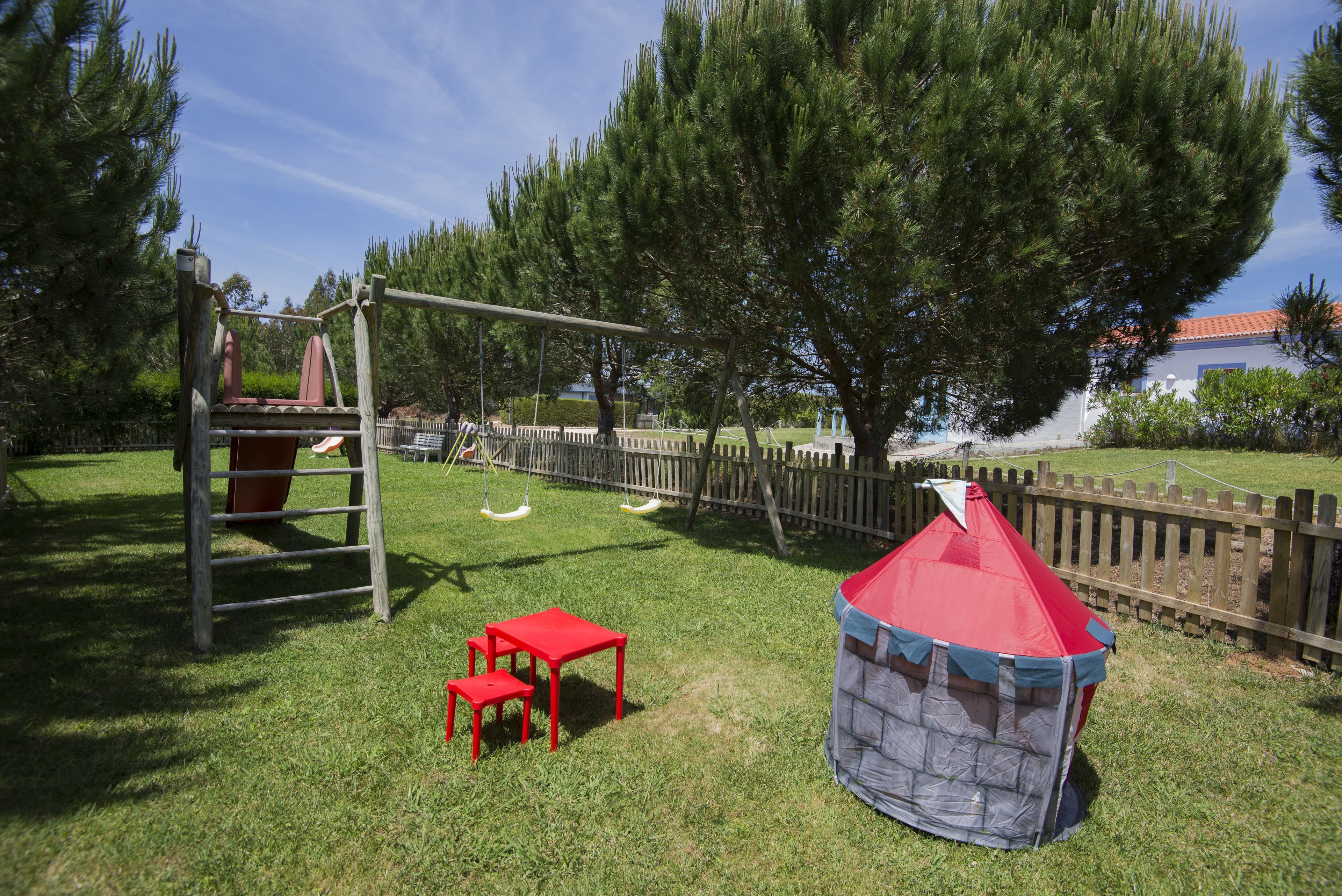 A playground with a swing set, red tables, and a play tent.
