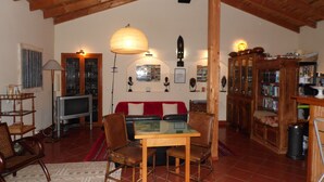 A cozy living room with a wooden ceiling, a red sofa, a glass-top coffee table, and a television. - Casa Vicentina (Aljezur)