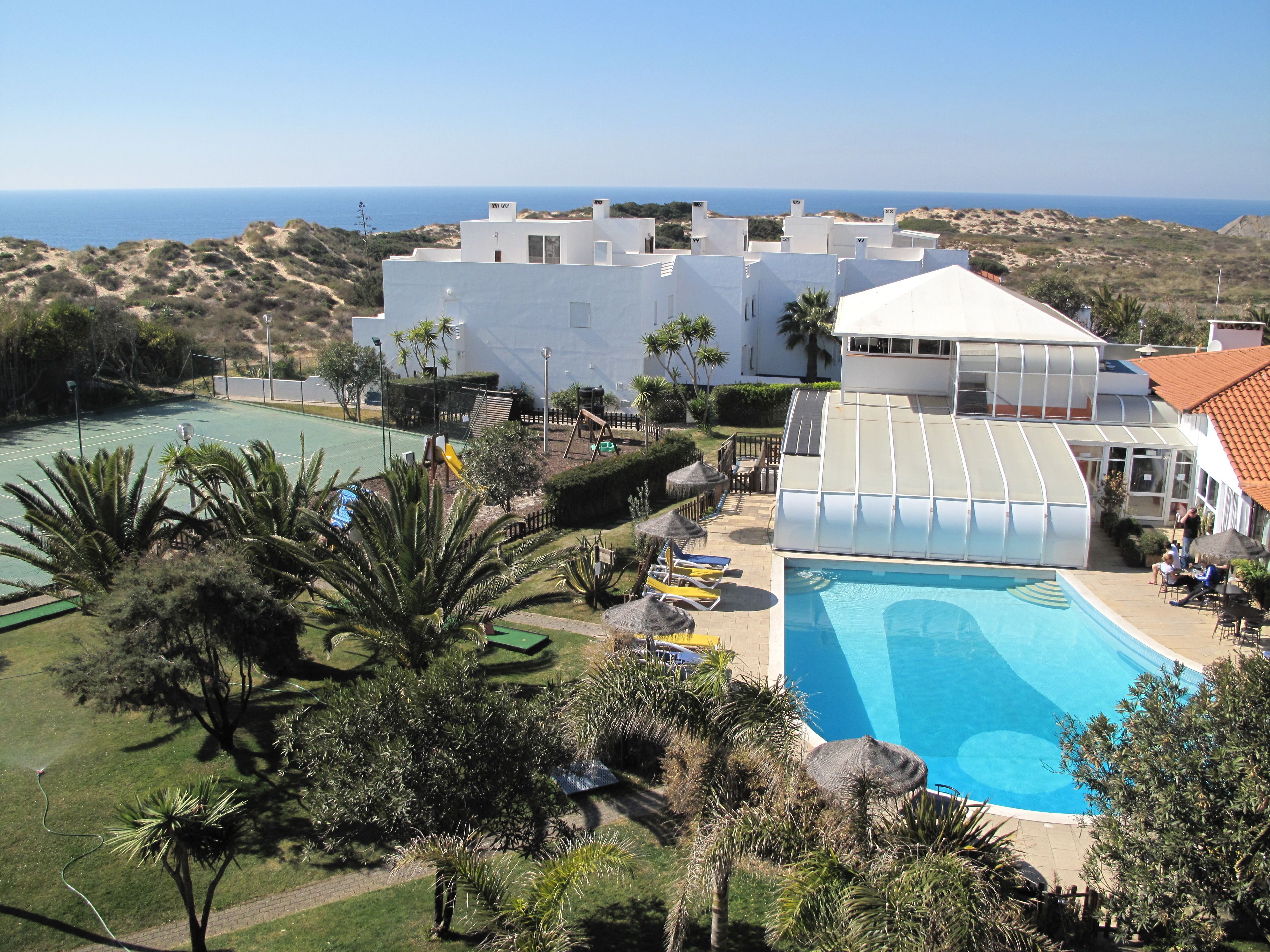 A resort with a swimming pool, tennis courts, and a view of the sea.
