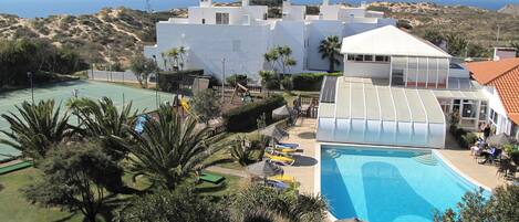 A resort with a swimming pool, tennis courts, and a view of the sea.