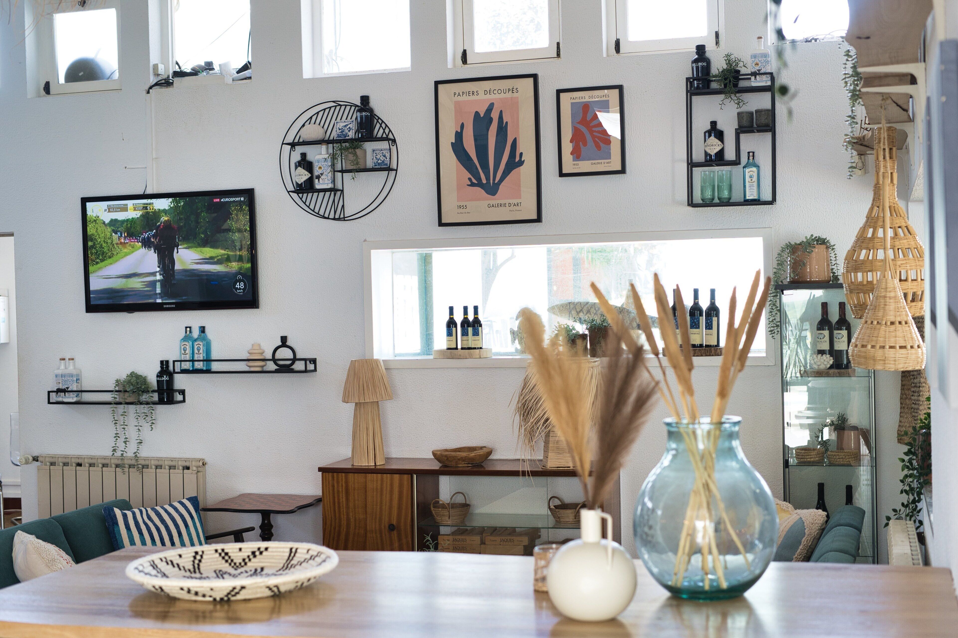 Ein Wohnzimmer mit Fernseher, Kunstwerken, Regalen mit Flaschen und einem Tisch mit Dekoration.