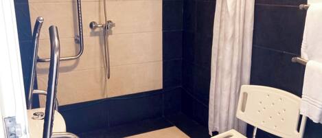 A modern bathroom with a walk-in shower, a toilet with a bidet attachment, a white chair, and a towel rack.