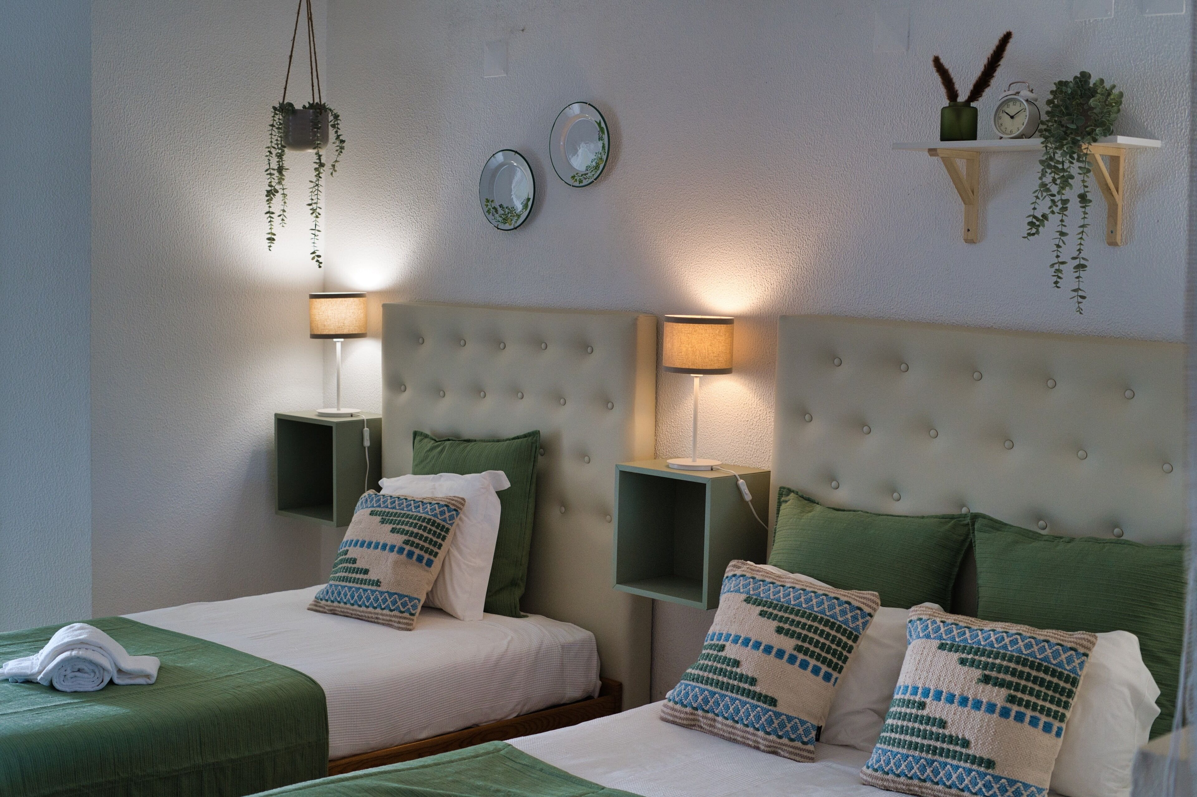 A hotel room with two beds, green bedding, a tufted headboard, bedside lamps, and wall-mounted mirrors.