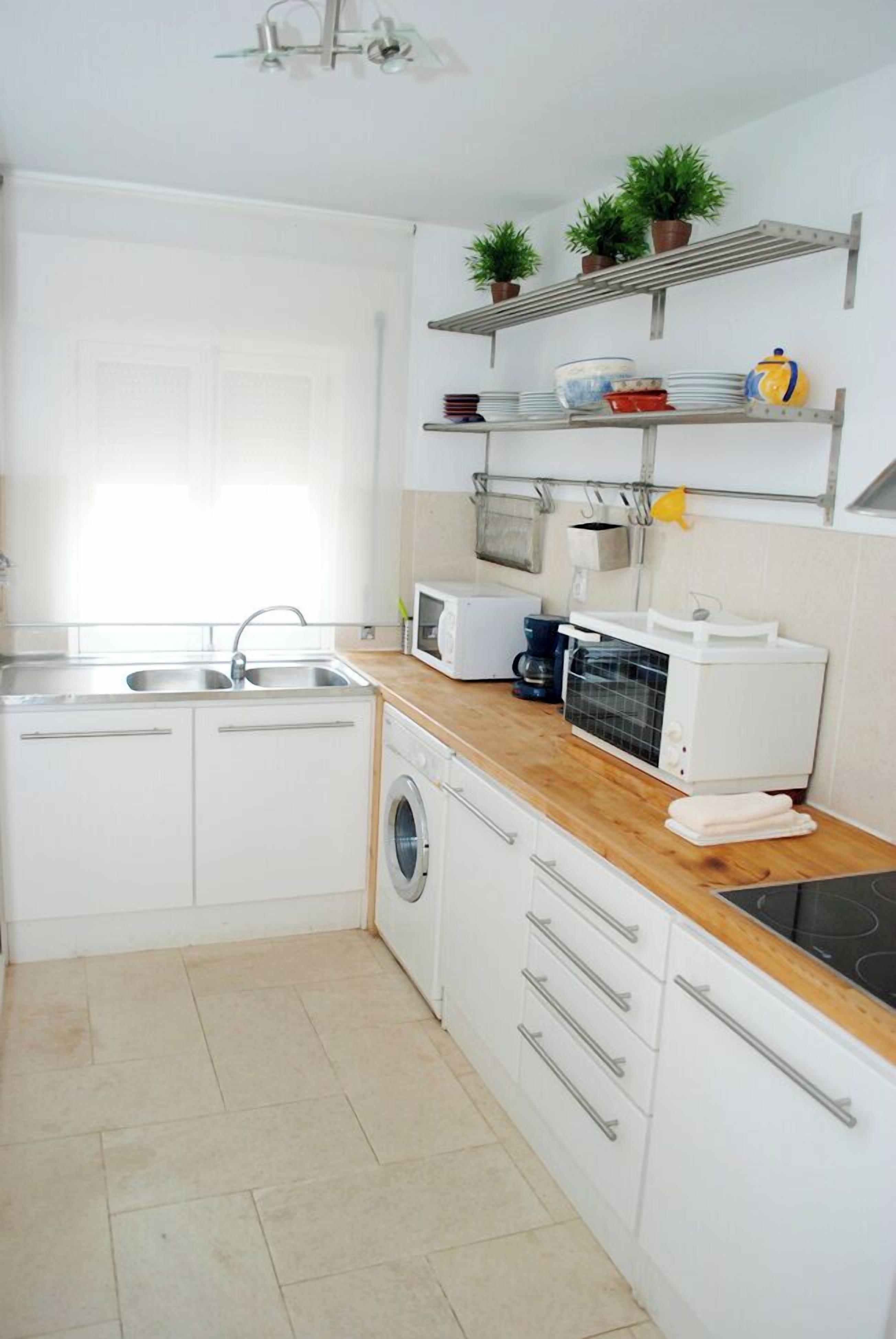 A modern kitchen with white cabinets, a wooden countertop, a washing machine, a microwave, and a coffee maker.