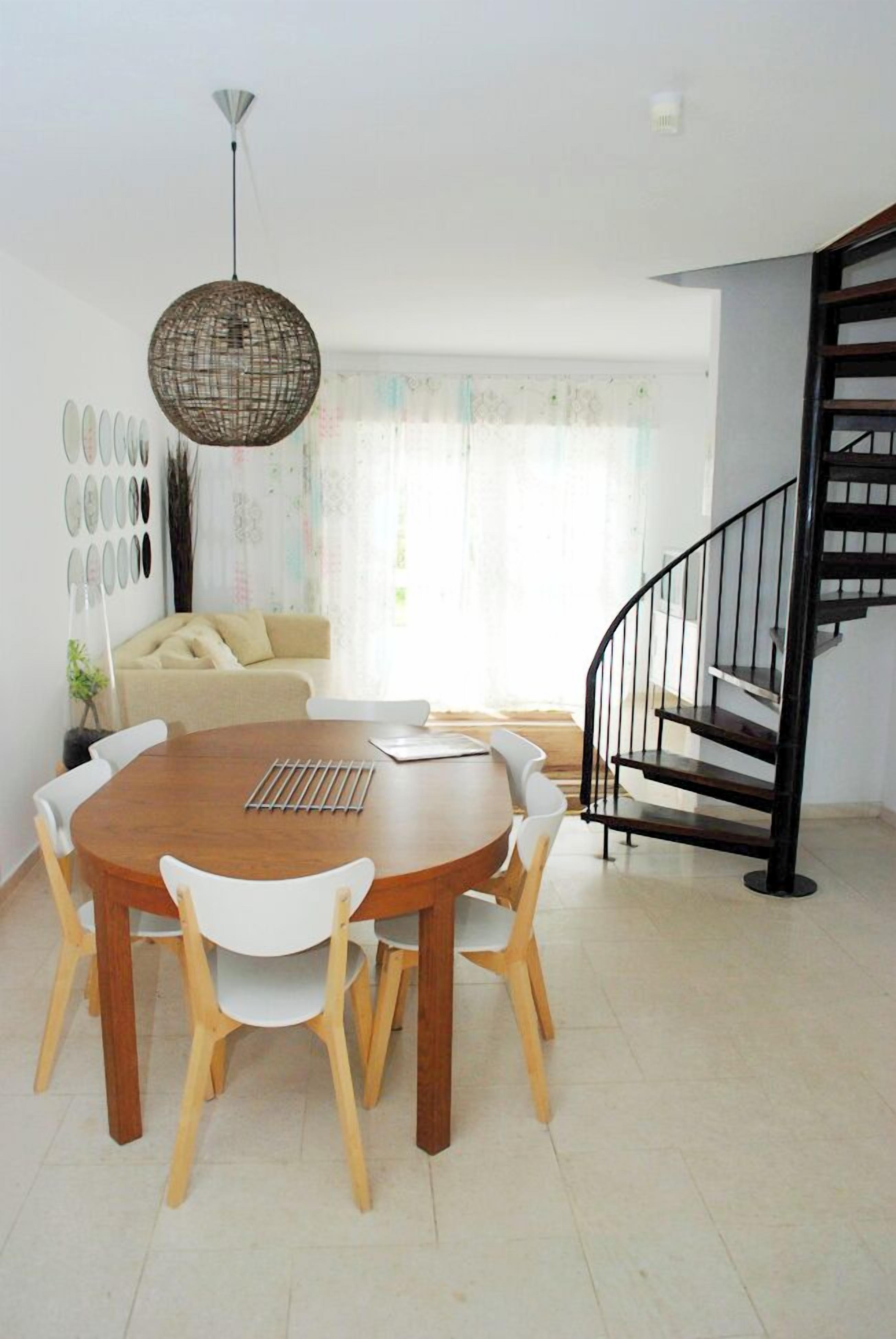 Un comedor con una mesa redonda de madera, sillas blancas y una lámpara colgante.