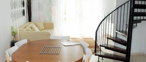 A dining area with a round wooden table, white chairs, and a hanging light fixture.