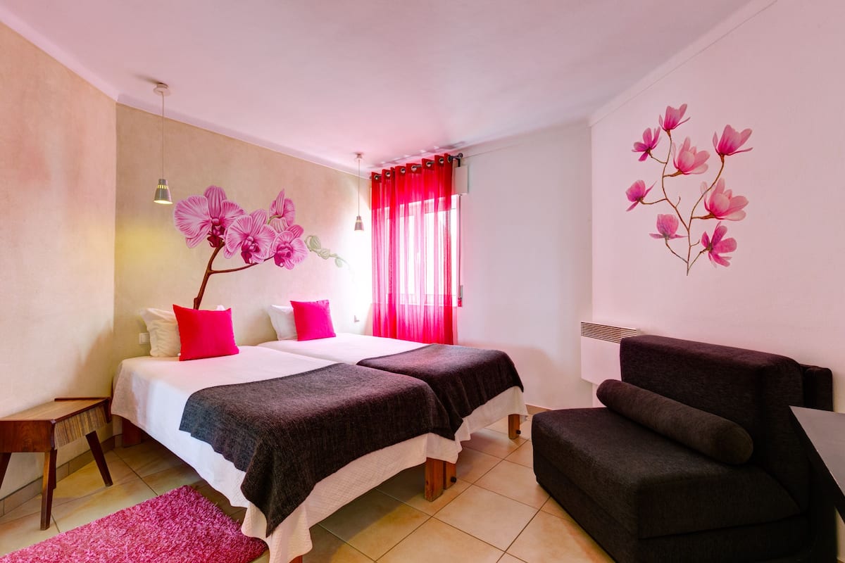 A bedroom with two beds, a sofa, a small table, and a decorative wall.