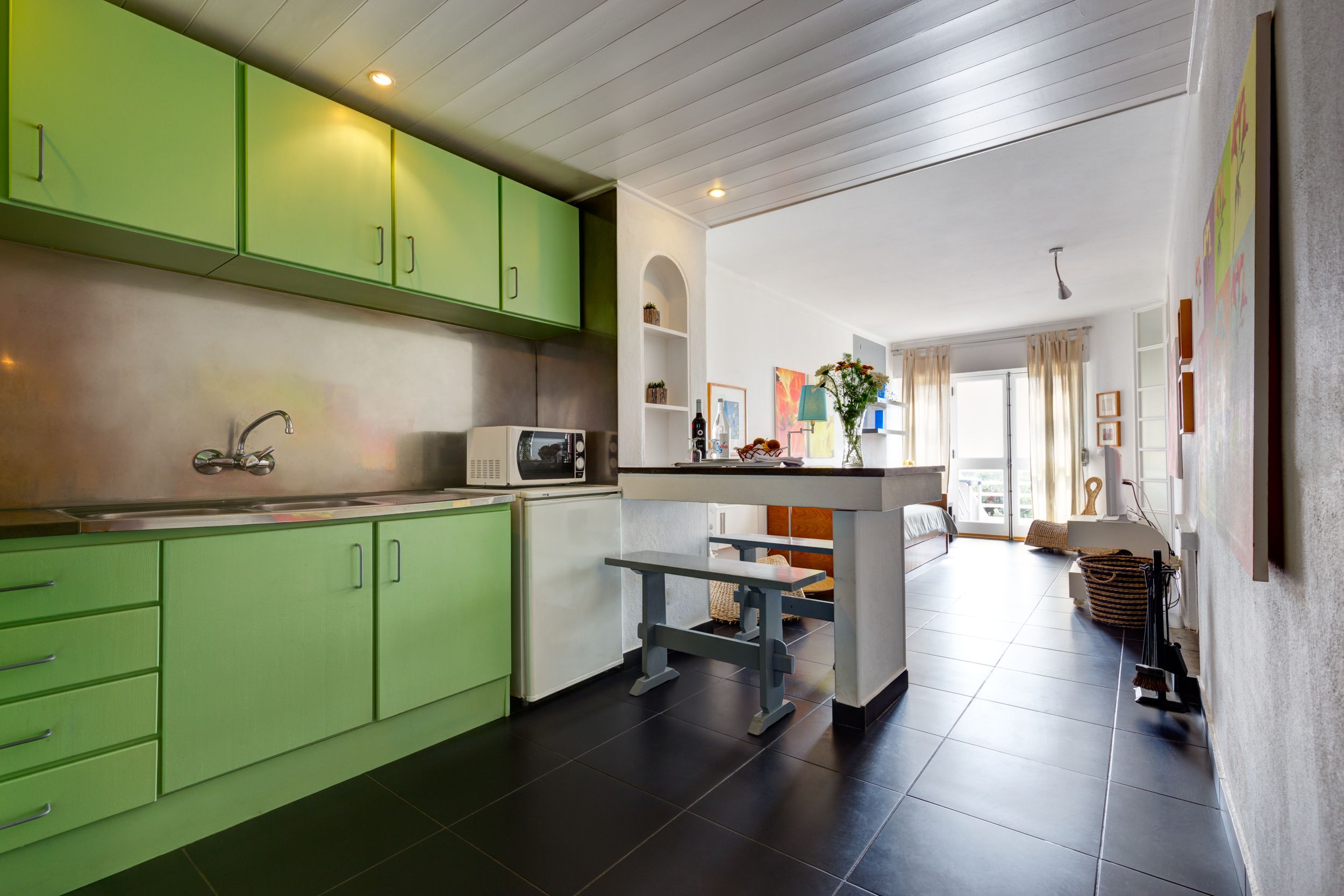 A modern kitchen with green cabinets, a central island, and a dining area with a bench.