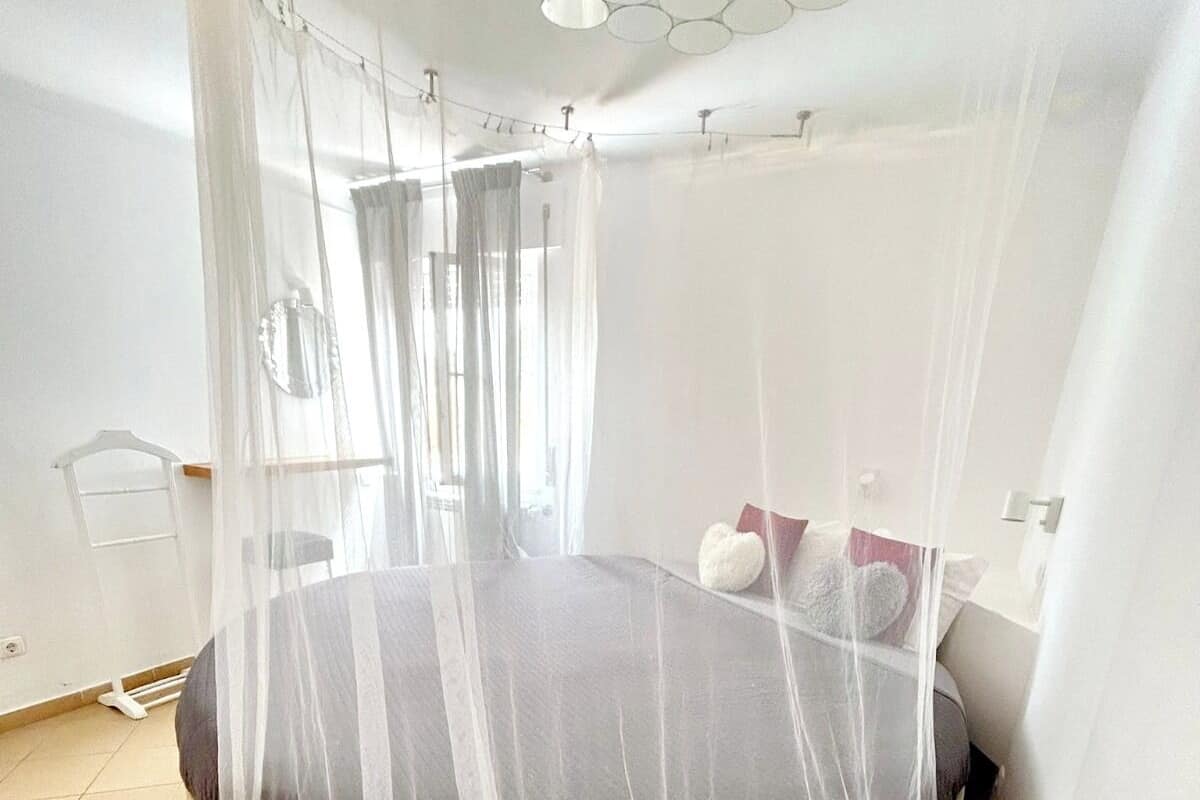 A bedroom with a bed covered by a sheer canopy, a round bedspread, and a white wall with a circular light fixture.