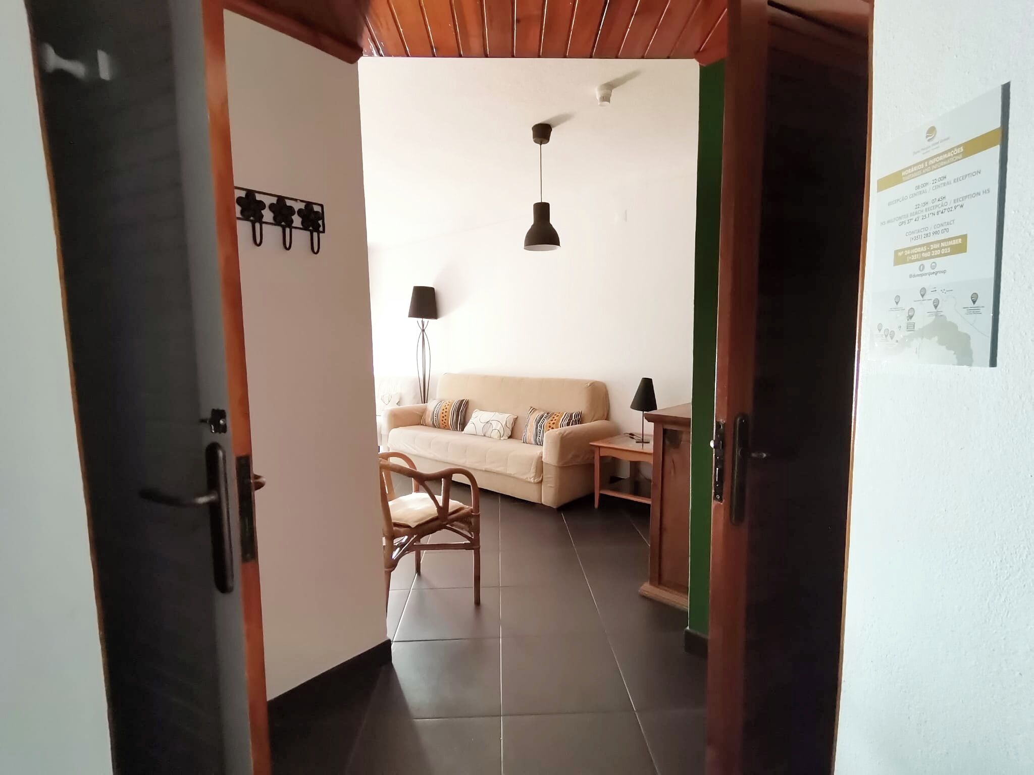 A hallway leading to a living area with a sofa, a chair, a lamp, and a small table.