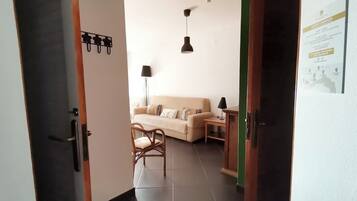 A hallway leading to a living area with a sofa, a chair, a lamp, and a small table.