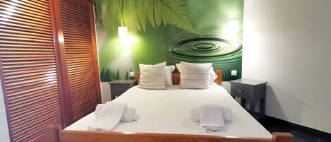 Una cama bien hecha con sábanas y almohadas blancas, un cabecero de madera y una pared con un mural de una hoja verde grande.