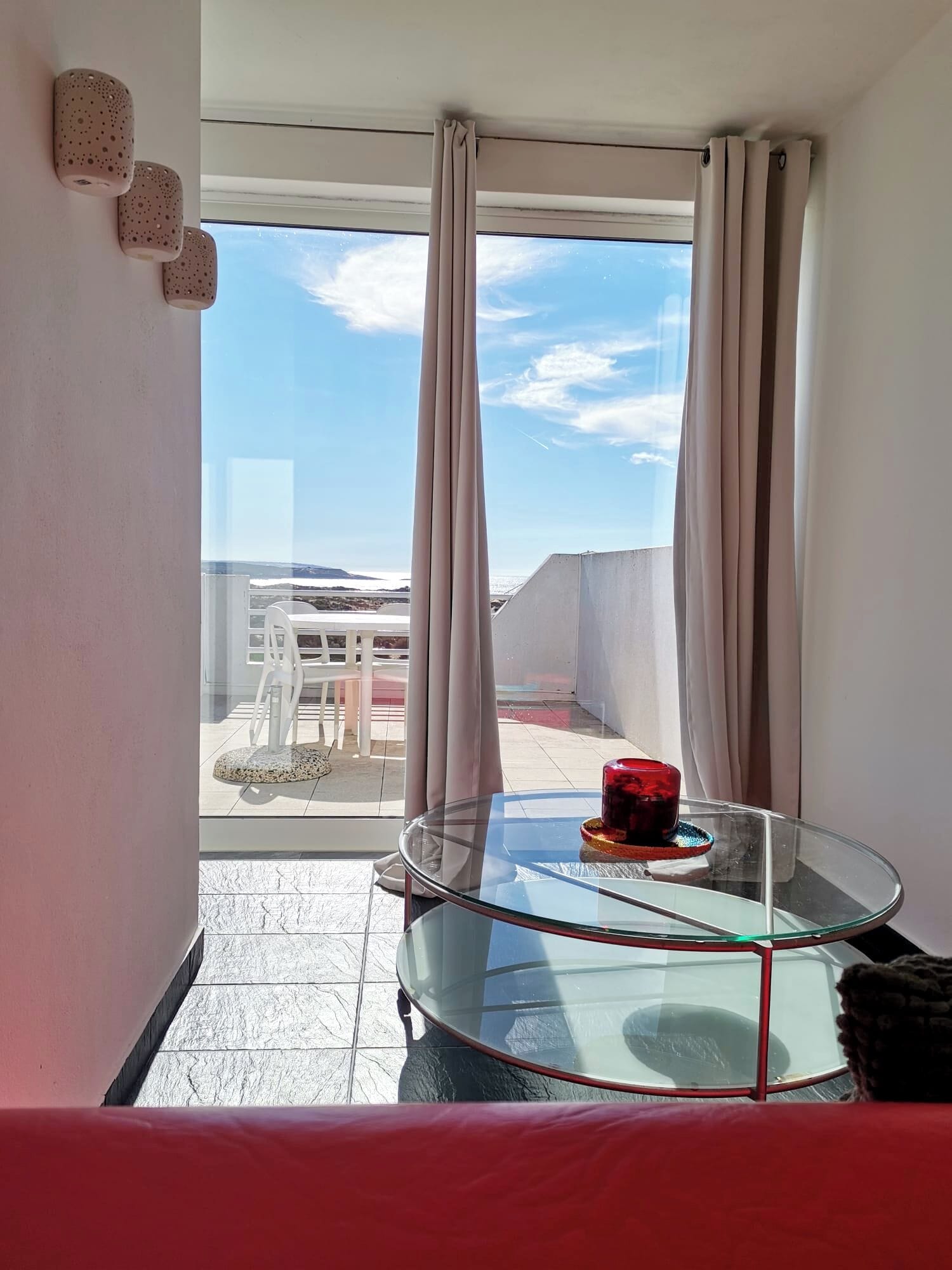 A balcony with a glass table, a red candle, and a view of the cityscape.