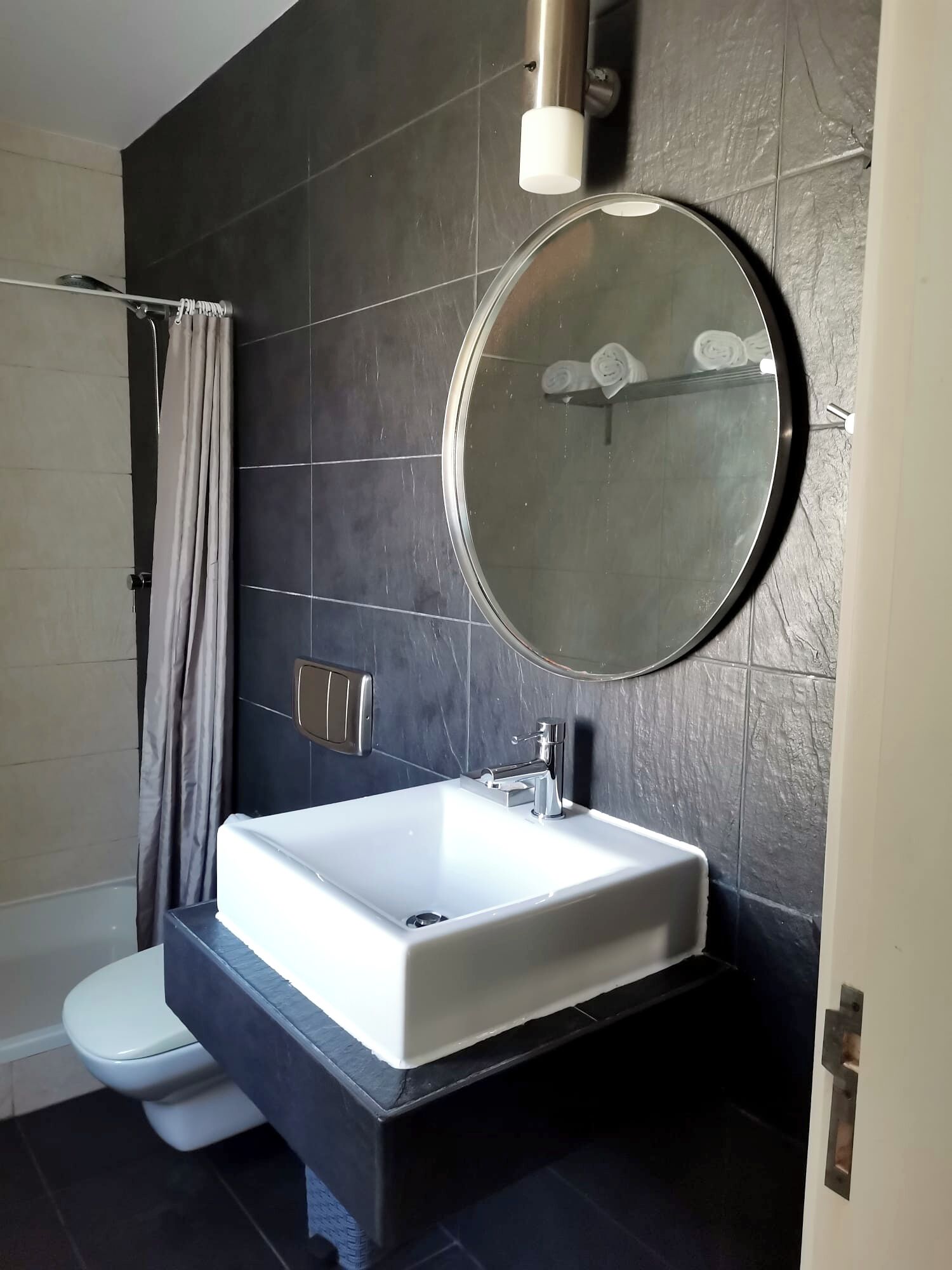 A modern bathroom with a large rectangular sink, a round mirror, and a toilet.