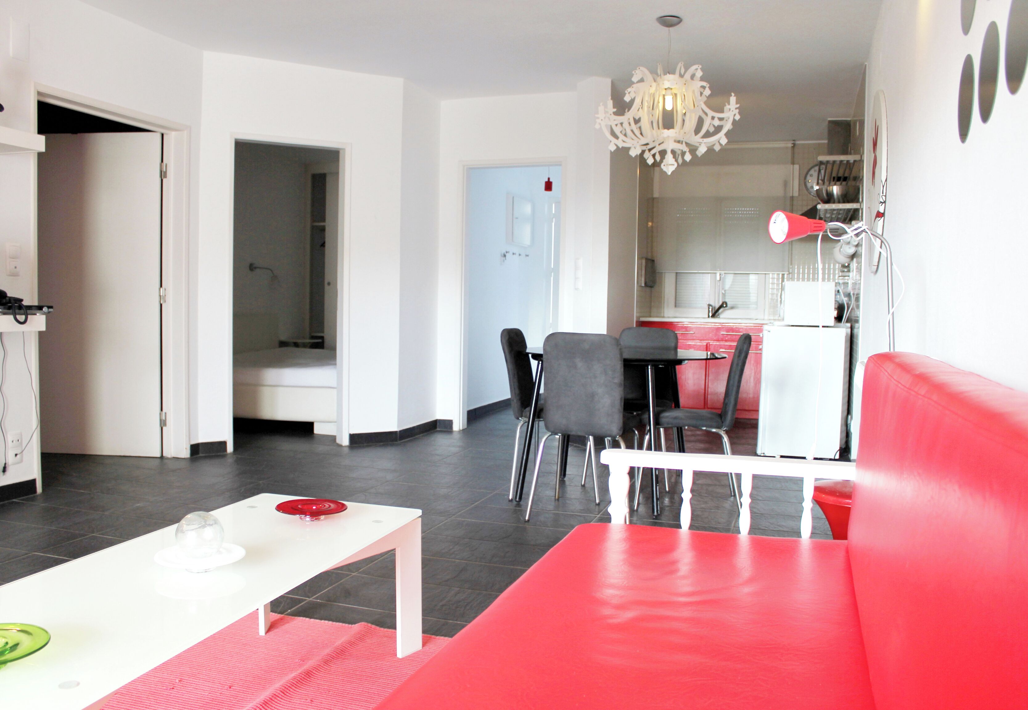 A modern living room with a red sofa, a white coffee table, and a dining area with a red table and chairs.