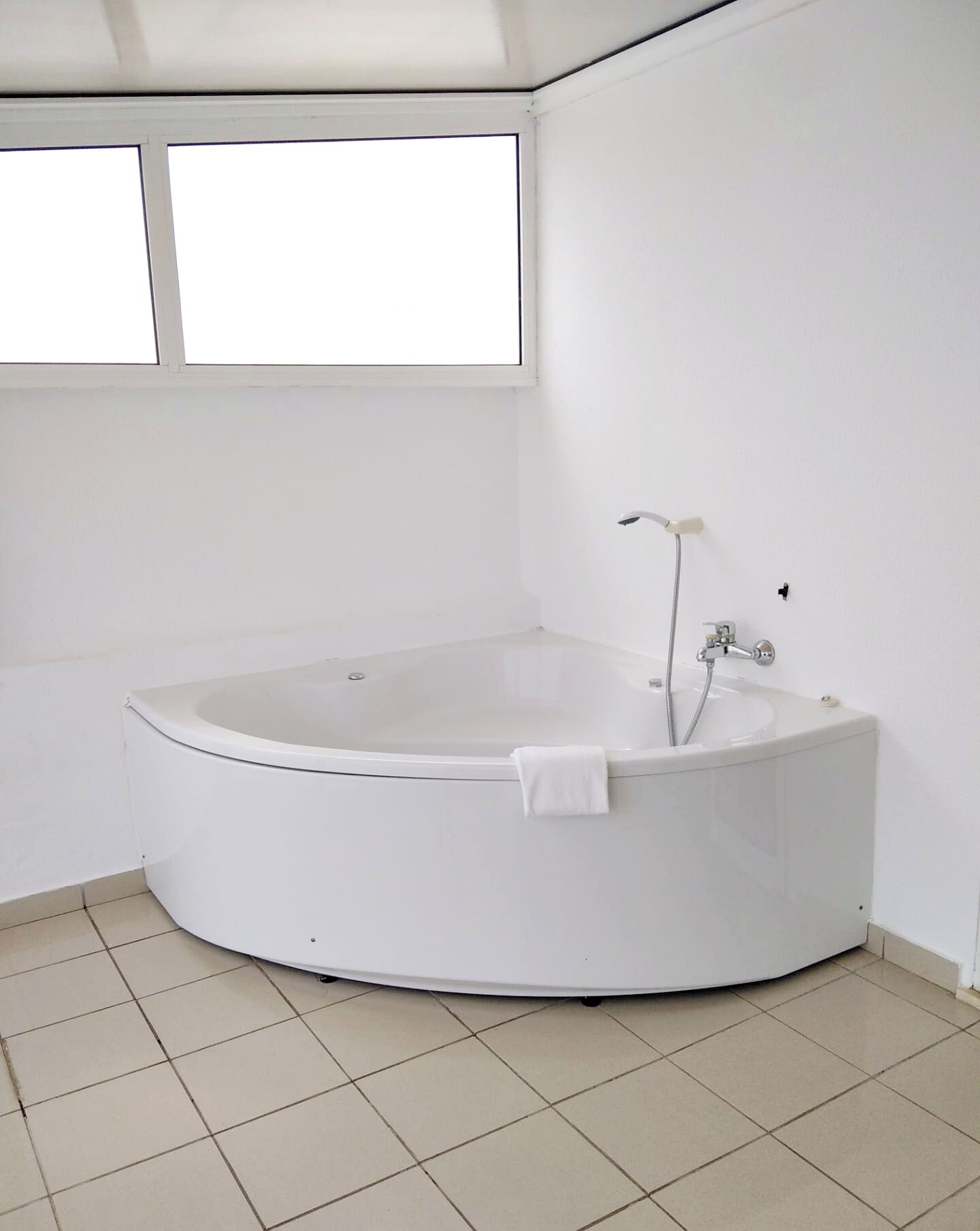 Une salle de bain blanche avec une baignoire sur pieds, une fenêtre et un sol carrelé.
