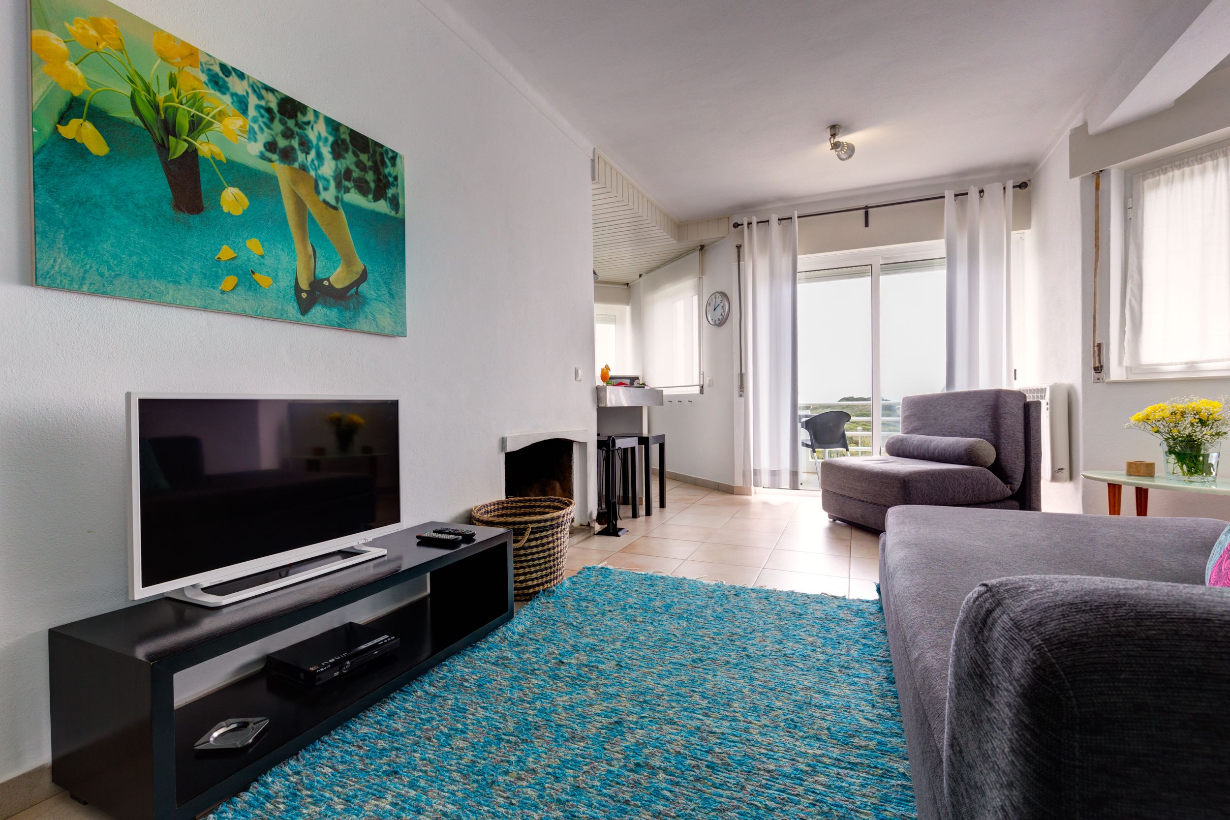 A modern living room with a flat-screen TV, a sofa, a coffee table, and a blue patterned rug.