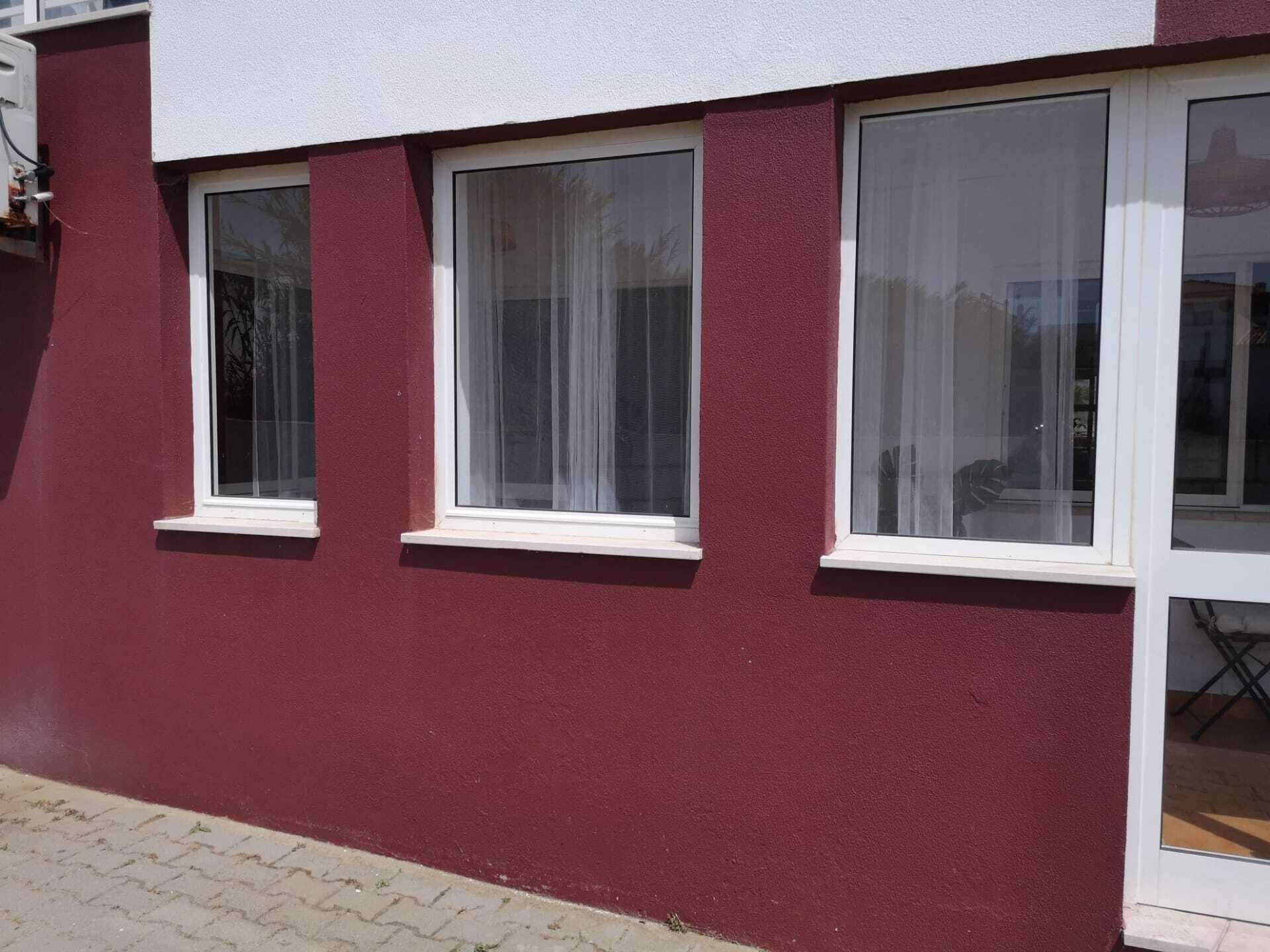 A building with three windows, each with white frames and white curtains.