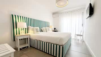 Une chambre d’hôtel avec une tête de lit à rayures, un lit avec une literie blanche, une table de chevet avec une lampe, une chaise et un téléviseur fixé au mur.