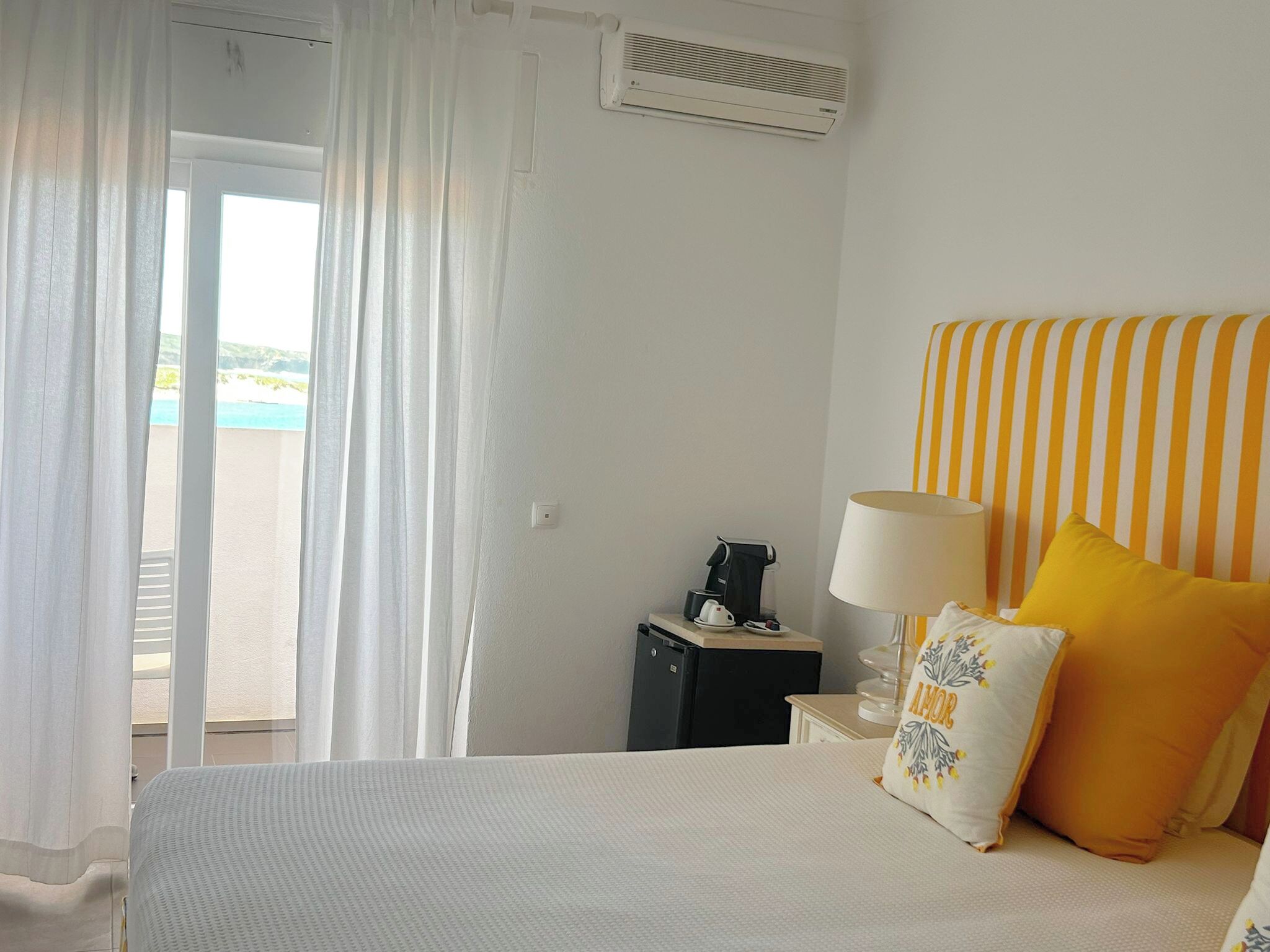 Una habitación de hotel con cama, mesita de noche, lámpara y vista a la playa.