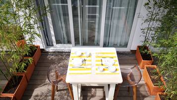 A table set for two with a yellow and white striped tablecloth, two chairs, and potted plants on either side.