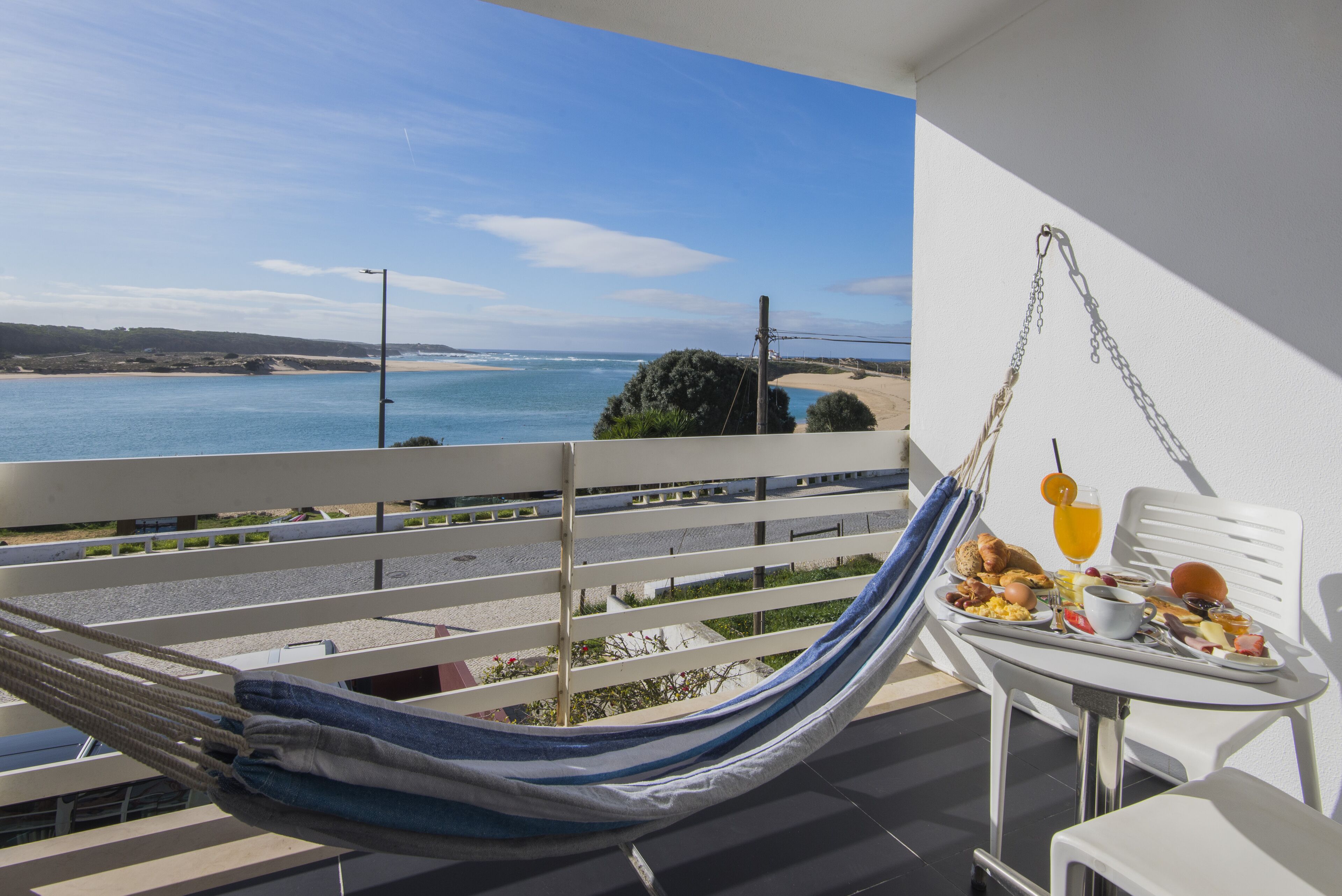 Un balcón con una hamaca, una mesa con desayuno y vista al mar.