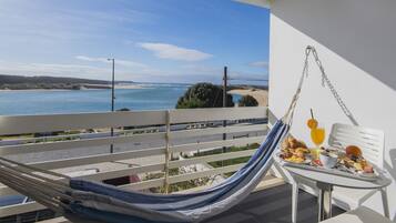Un balcón con una hamaca, una mesa con desayuno y vista al mar.